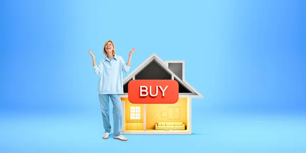 笑着站在房子旁边的年轻的欧洲女人 带有蓝色背景的购买标志 房地产采购的概念 — 图库照片