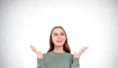 Şaşkın ya da şaşkın kadın portresi sıradan bir kazakla, elleri boş fotokopi alanı gri beton arka planda. Fikir kavramı, plan, başarı ve kazanma