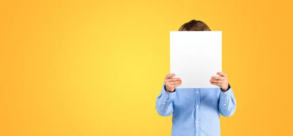 Child hiding face with mockup empty blank poster, copy space yellow empty background. Concept of emotion, feelings, idea, ad, announcement, marketing or sale
