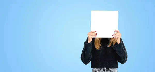 Young woman hiding face with mockup empty blank poster, wide format empty blue copy space background. Concept of emotion, plan, idea, ad, marketing or sale