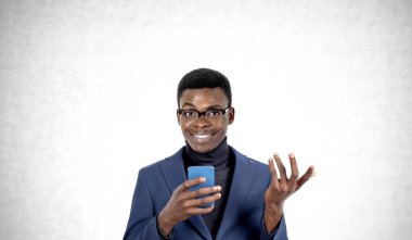 Telefonla çalışan gülümseyen Afrikalı işadamı dostça bir el hareketi yapıyor. Uzay gri duvar arkaplanını kopyala. İş ağı, sosyal medya ve iletişim kavramı