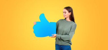 Gülümseyen genç bir kadın mavi başparmağıyla turuncu arka planda duran bir pankart gösteriyor. Geri bildirim kavramı, sosyal medya, iyi seçim, gibi ve değerlendirme