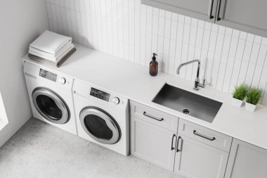 Üst kattaki çamaşırhanenin içinde lavabo, sabun şişesi ve beton zeminde iki çamaşır makinesi var. Minimalist dolap ve havlular tezgahın üstünde. 3B görüntüleme