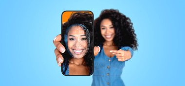 Gülümseyen siyahi kadın, telefonu yüzüyle ve biyometrik taramasıyla işaret ediyor, mavi arka plan. Kişisel bilgi koruma ve kimlik doğrulama kavramı