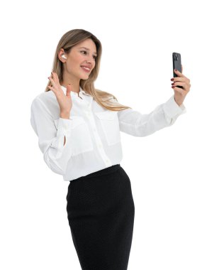 Beyaz gömlekli ve siyah etekli, beyaz arka planda soyutlanmış bir kadın selfie çekiyor. İletişim ve modern teknoloji kavramı