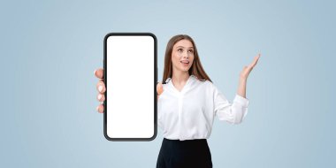 Büyük, boş bir akıllı telefon ekranı sunan bir kadın, bir eliyle mavi bir arkaplana işaret ediyor. İş veya reklam kullanımı için dijital şablon kavramı