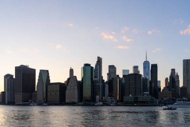 Günbatımında New York şehrinin ufuk çizgisi, yüksek gökdelenler ve sakin bir rıhtım. Sakin bir gökyüzü arka planına sahip şehir manzarası. Şehir hayatı ve mimarisi kavramı