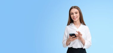 Gülümseyen bir kadın beyaz bluz giyen bir akıllı telefonu açık mavi arka planda tutar. Görüntü, iş ve teknoloji kavramları için ideal geniş kopyalama alanına sahiptir.