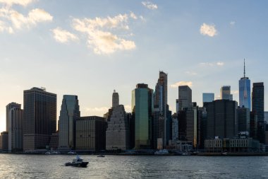 Manhattan rıhtımının silueti, gün batımında berrak bir gökyüzünün altında suya yansıyan ikonik binalar. Kentsel güzellik ve modern mimari kavramı