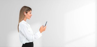 Kablosuz kulaklık takan, beyaz arka planda duran akıllı telefon tutan bir kadın. Geniş kopya alanına sahip teknoloji ve iletişim konsepti