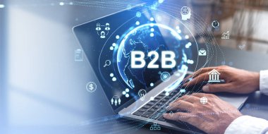 B2B simgeleri ve mavi tonlu arka planda dijital küre olan bir dizüstü bilgisayarda yazan bir işadamı. İş teknolojisi ve ağ kurma kavramı
