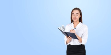 Bir iş kadını mavi arka planda dururken deftere notlar yazıyor. Profesyonellik ve üretkenlik kavramı