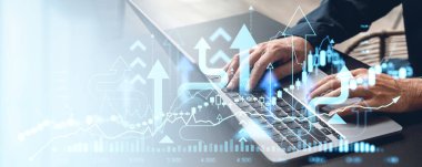 Finans grafikleri, okları ve çizelgeleri hafif arka planda olan bir dizüstü bilgisayarın klavyesinde yazan bir iş adamı. Borsa analizi ve finansal başarı kavramı