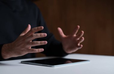 Beyaz bir yüzeye yerleştirilmiş tabletin üzerinde el kol hareketleri. Koyu renk bir kıyafet giyiyor. İletişim ve teknoloji kavramı