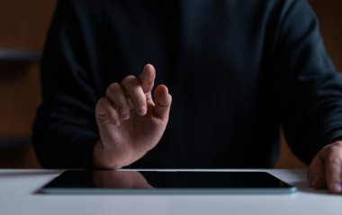 Koyu arkaplanda tabletle etkileşime giren bir elin yakın plan çekimi. Teknoloji, dokunmatik ekran ve dijital arayüz kavramı