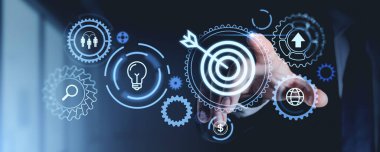 Bir el, dişliler, oklar ve ampul simgeleriyle çevrili bir hedef ikonu işaret ediyor. Karanlık bir arkaplanda gelecek tasarımı, başarı ve fikirleri temsil ediyor.