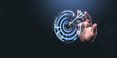 Bir adam karanlık bir arkaplanda okla fütürist bir dijital hedef simgesine dokunmak için uzanır, başarıyı ve stratejiyi simgeler.