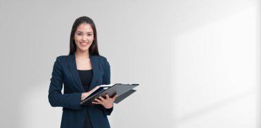 A smiling businesswoman in formal attire holds a clipboard. She stands confidently against a light background, symbolizing professionalism and success clipart