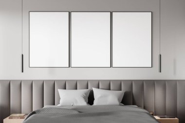 Yastıklı, modern ışıklandırmalı ve minimalist dekorlu şık bir yatağın üstündeki gri duvarda üç boş poster. İç tasarım kavramı. 3B Hazırlama