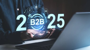 Elinde B2B 2025 ve strateji sembolleri olan fütürist hologramlar tutan bir iş adamı, karanlık bir arkaplanda duruyor. İş planlama kavramı