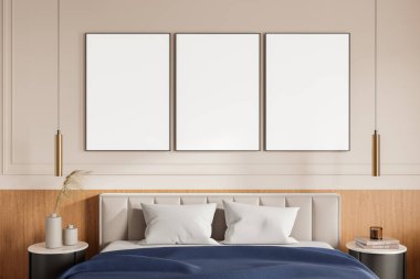 Three empty framed posters displayed on a beige wall above a bed with cushions, side tables, and pendant lights in a modern bedroom interior concept. 3D Rendering. clipart