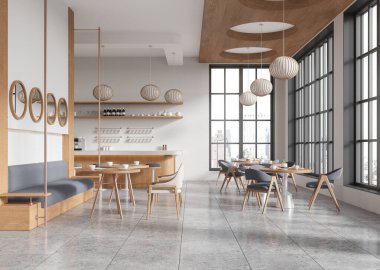Ahşap sandalyeleri, masaları, gri yastıklı koltukları ve kolye ışıkları olan modern bir kafe. Büyük pencereler doğal ışık getirir. Sıcak, minimalist tasarım. 3B Hazırlama