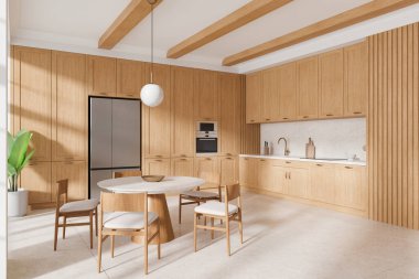 Ahşap dolapları, yuvarlak yemek masası, sandalyeleri ve tavan kirişleri olan modern bir mutfak. Parlak ışıklandırma, açık renkli zemin ve köşede bitki. 3B Hazırlama