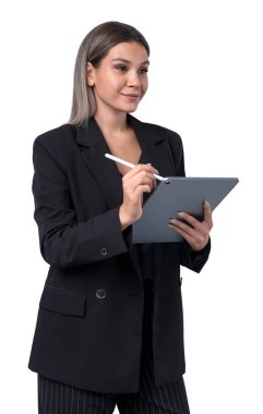 A businesswoman wearing a suit is holding a tablet and writing with a stylus. She is standing against a white background. Concept of technology and work clipart