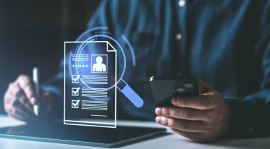 Bir kişi bir telefon ve Stylus tutuyor, yüzen holografik arayüzle etkileşime geçiyor. Karanlık arka plan. Dijital eleman alma ve işe alma kavramı