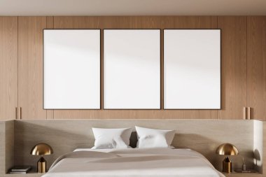Modern bir yatak odasındaki ahşap duvarlı bir yatağın üzerinde asılı üç boş çerçeveli poster. Tarafsız yatak örtüsü ve komodinlerin üzerinde altın lambalar. Poster şablonu. 3B Hazırlama.