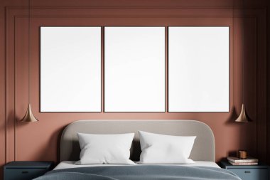 Modern bir yatağın üzerinde, beyaz yastıklı, kolye lambalı ve gösterişli komodinli sıcak kahverengi bir duvarda üç boş çerçeveli poster. 3B Hazırlama