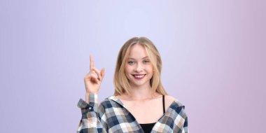 Gülümseyen bir kadın parmağını yukarı kaldırıyor, kareli bir gömlek giyiyor, pastel bir arka plana karşı poz veriyor, fikir ya da düşünce konsepti
