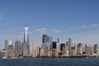 New York City 'nin ikonik Manhattan gökdelenlerinin panoramik manzarası açık mavi gökdelenlerin altında, suyun diğer tarafından görülüyor.