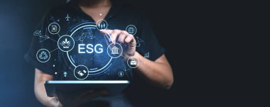 El, koyu bir arka planda, sürdürülebilirliği, sosyal sorumluluğu ve yönetimi temsil eden, parlayan ESG dijital simgeleriyle etkileşir. Yenilik kavramı