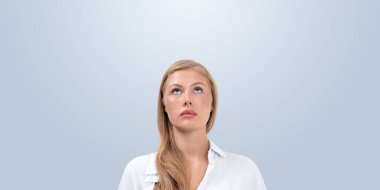 Woman with blonde hair and white shirt looking upwards on a light blue background. Concept of thinking, inspiration, or curiosity clipart