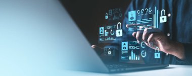 Bir kişi koyu arkaplanda yüzen holografik kilit, veri grafikleri ve kullanıcı profilleri olan bir dizüstü bilgisayar kullanıyor. Siber güvenlik kavramı