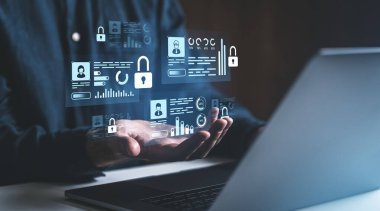 Bilgisayarın önünde tutulan ve siber güvenlik ve veri korumasını temsil eden kilitleri ve analitiği olan dijital veri simgeleri