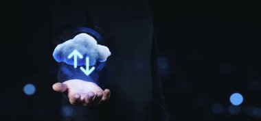 Yukarı ve aşağı oklarla parlayan bir bulutu tutan, karanlık bir arkaplanda bulut depolama ve veri transferini sembolize eden bir el. Çevrimiçi veri değişimi kavramı