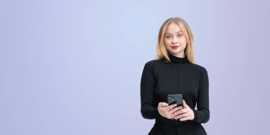 Siyah kıyafetli şık bir kadın elinde akıllı telefon, hafif bir arka planda duruyor. Teknoloji, güven ve iletişim kavramı