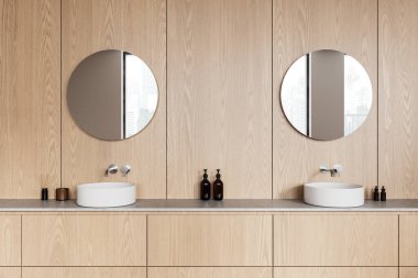 Çift gösterişli, ahşap dolapları, yuvarlak aynaları ve beyaz lavaboları olan zarif bir banyo. Doğal ahşap kaplamalı minimalist modern tasarım. 3B Hazırlama