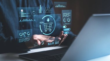 Karanlık bir arka planda veri analizi grafikleri olan holografik bir alışveriş arabasını tutan bir el. Çevrimiçi iş kavramı