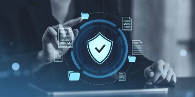 İş adamı, bir kalkan simgesi ve veri dosyalarını gösteren dijital bir siber güvenlik arayüzü ile etkileşimde. Koyu arkaplanda gelecek biçimi