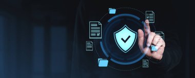 Karanlık bir arkaplanda veri güvenlik sembolleriyle çevrili gelecekteki dijital kalkan ikonu ile el etkileşimi, siber güvenlik korumasını temsil ediyor.