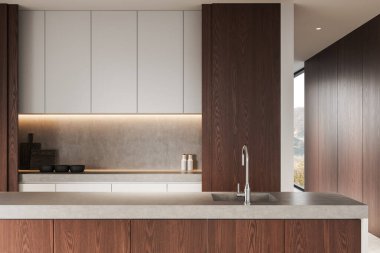 Ahşap paneller, beton tezgahlar ve minimalist beyaz dolaplarla donatılmış modern bir mutfak. Ilık ışıklandırma ve parlak musluk atmosferi güçlendirir. 3B Hazırlama