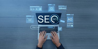 Eller, SEO holografik arayüzü olan bir dizüstü bilgisayarda yazıyor ve ahşap bir masada arama ile ilgili simgeleri gösteriyor. Çevrimiçi pazarlama, analiz ve başarı kavramı