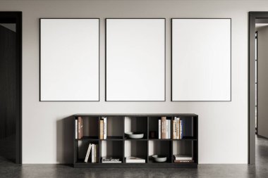 Modern bir kitaplığın üstündeki beyaz bir duvarda, içinde temiz iç dekorasyon ve kitaplar bulunan üç boş poster. 3B Hazırlama