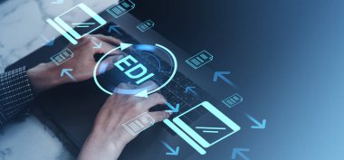 Dijital işlemleri ve otomasyonu sembolize eden elektronik veri aktarımı (EDI) belgeleri ve okları dijital simgeleyen bir dizüstü bilgisayarda yazı yazan eller