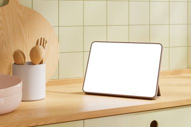 Tablet, ahşap mutfak tezgahında boş bir ekran, mutfak aletleri ve kâseleriyle çevrili. Arka planda açık yeşil fayanslı duvar var. Modern dijital model. 3B Hazırlama