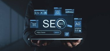 Dijital pazarlama teknolojisini temsil eden arama, reklam, analitik ve web elementleri de dahil olmak üzere SEO ile ilgili sanal simgelerle dolu bir tablet tutan eller.