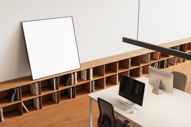 Modern ofis içinde ahşap bir kitaplığa yaslanmış boş çerçeveli poster, temiz beyaz bir masa, bilgisayar monitörleri ve çalışma alanındaki sandalyeler. 3B Hazırlama